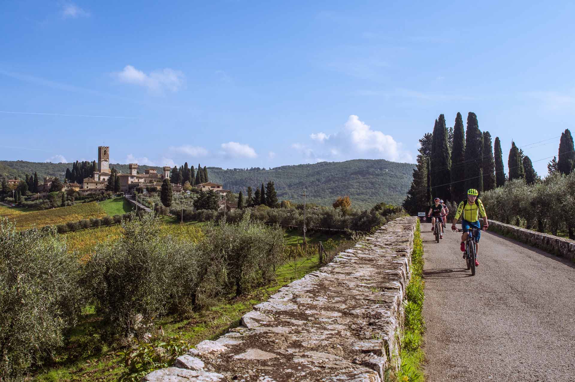 Tre ciclisti percorrono una strada panoramica nel cuore del Chianti, con un borgo toscano sullo sfondo