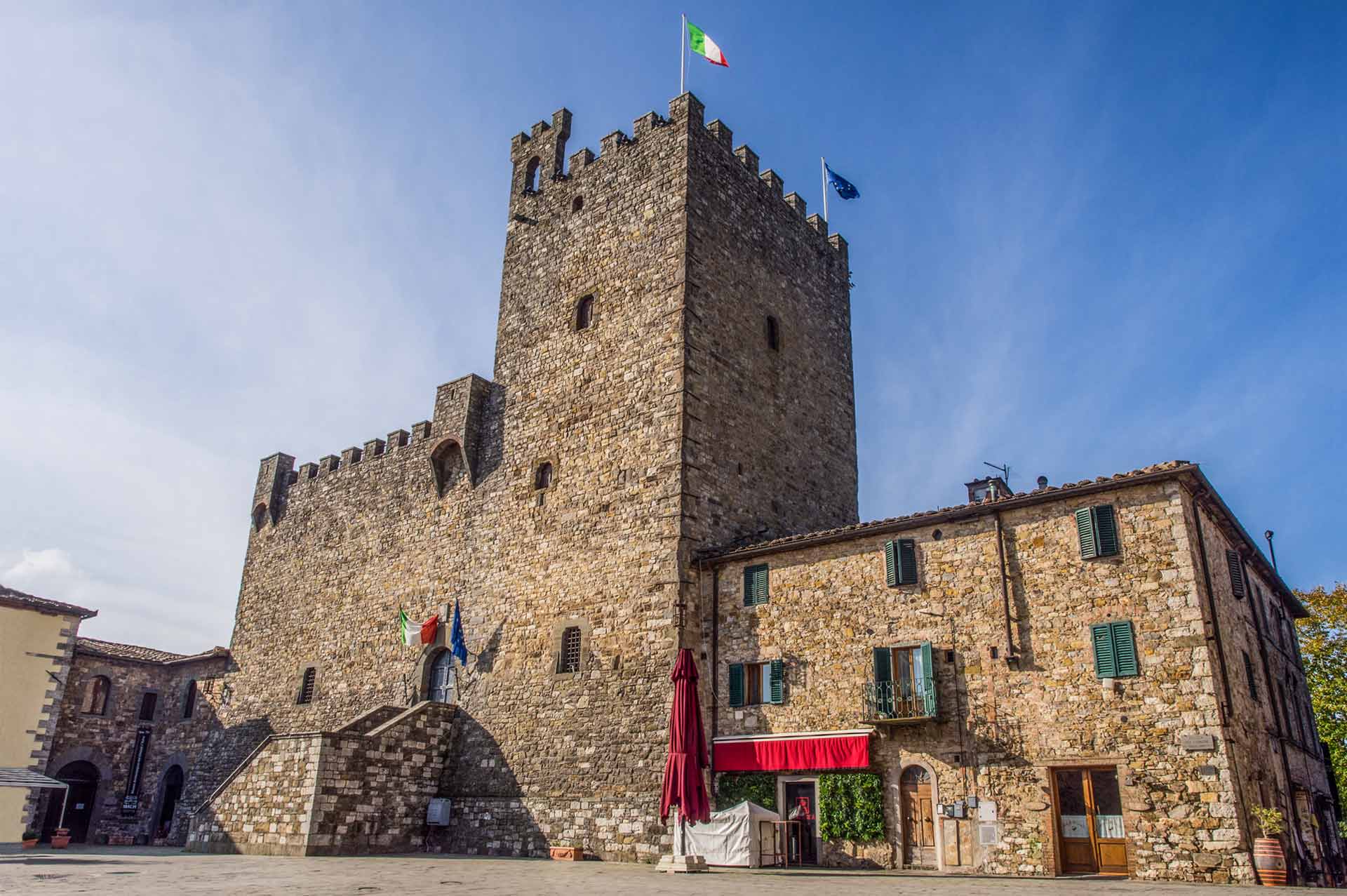 Storico castello in pietra con bandiere italiane ed europee a Castellina in Chianti, in Toscana