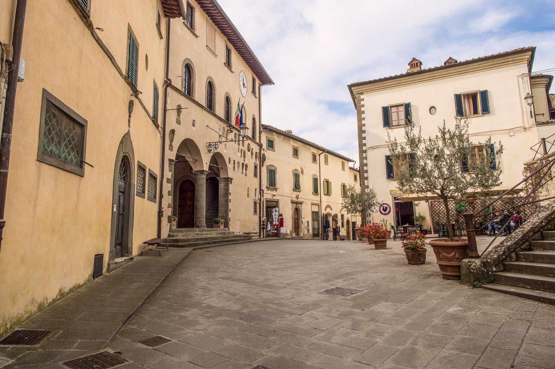Piccola piazza di un borgo nel Chianti con edifici storici, fioriere e ristorante all’aperto