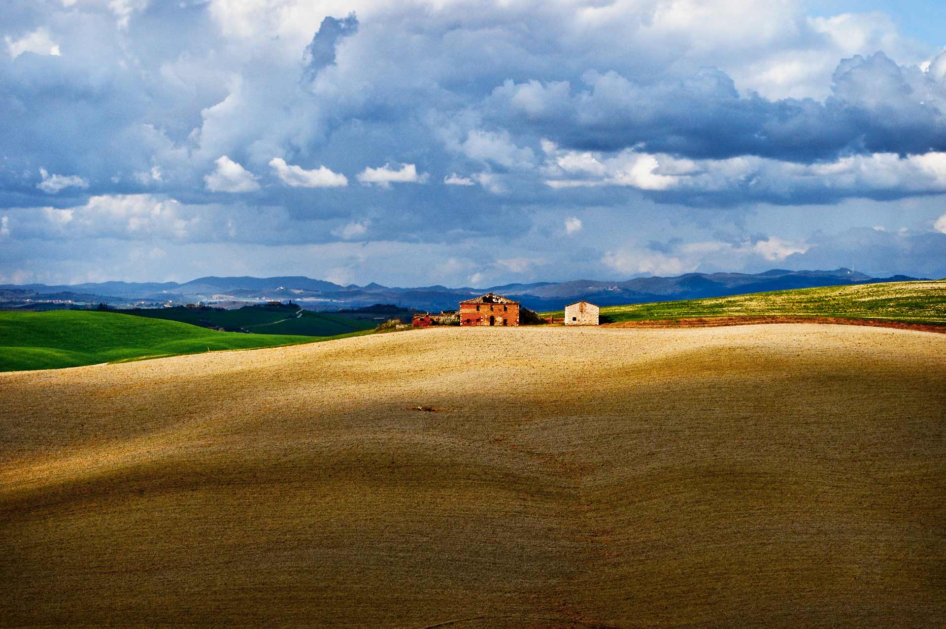 Paesaggio delle Crete Senesi con casali rurali e cielo nuvoloso, tipico della campagna toscana nei dintorni di Siena