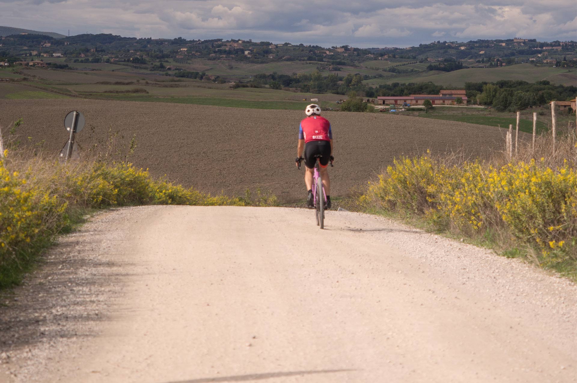 Un ciclista percorre una strada bianca tra prati verdi in Toscana